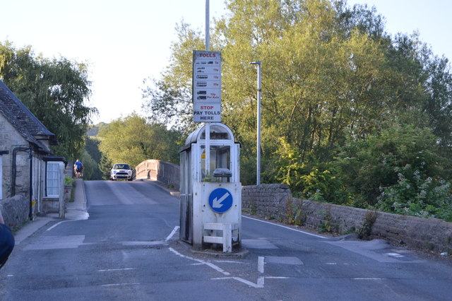 A small toll booth in the middle of a road, with a bridge behind it.